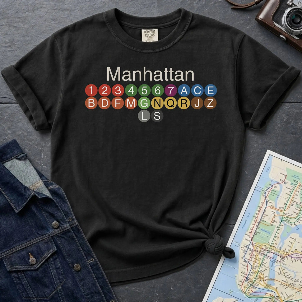 Black Comfort Colors t-shirt featuring a minimalist Manhattan subway line graphic with colorful NYC train icons.