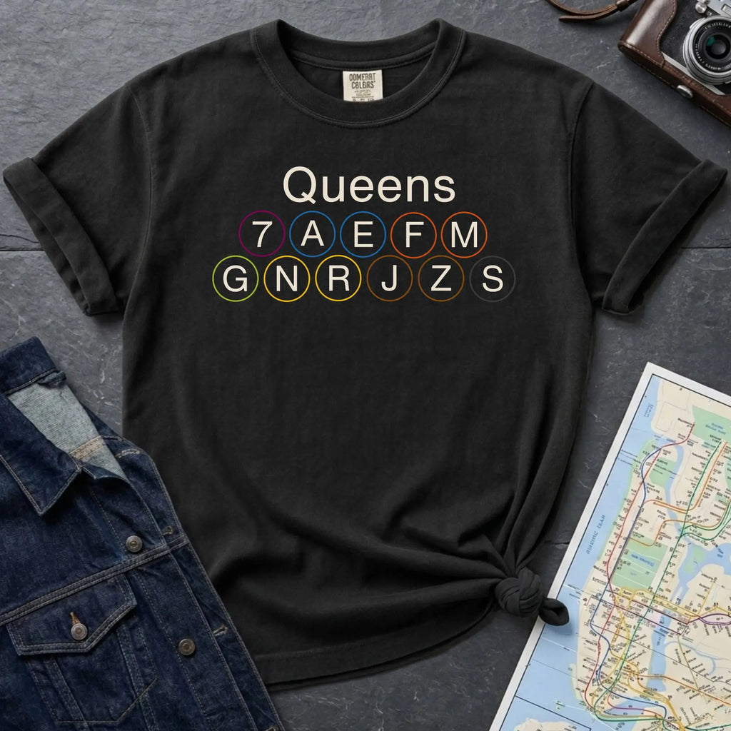 Black Comfort Colors t-shirt featuring a minimalist Queens subway line graphic with Queens text and classic NYC train icons.