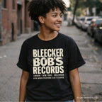 Woman wearing a black Comfort Colors t-shirt with Bleecker Bob's Records in large distressed block lettering, London, New York, Hollywood and Open When Everyone Else Is Closed below, while walking down a NYC street.