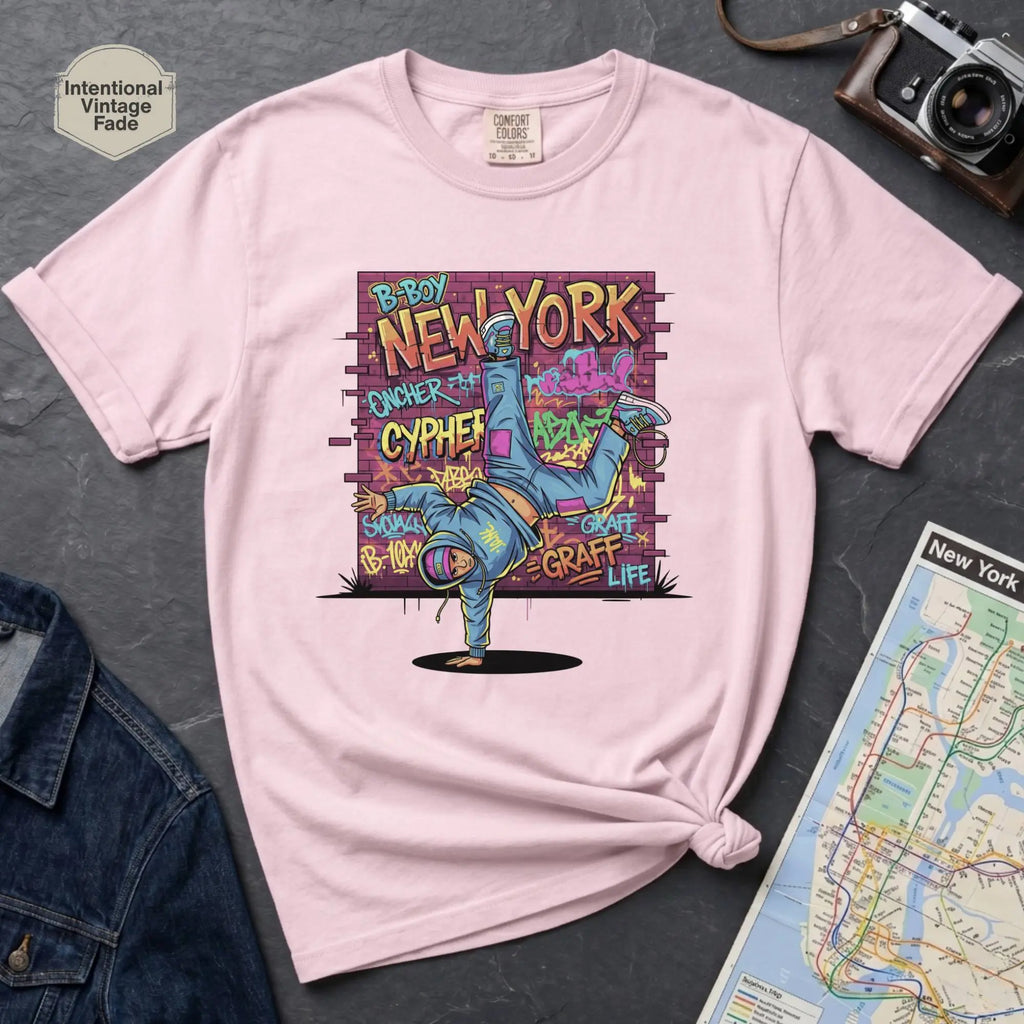Pink t-shirt with a colorful graphic design featuring a breakdancer and text on a dark surface with a denim jacket and a map.
