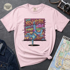 Pink t-shirt with a colorful graphic design featuring a breakdancer and text on a dark surface with a denim jacket and a map.