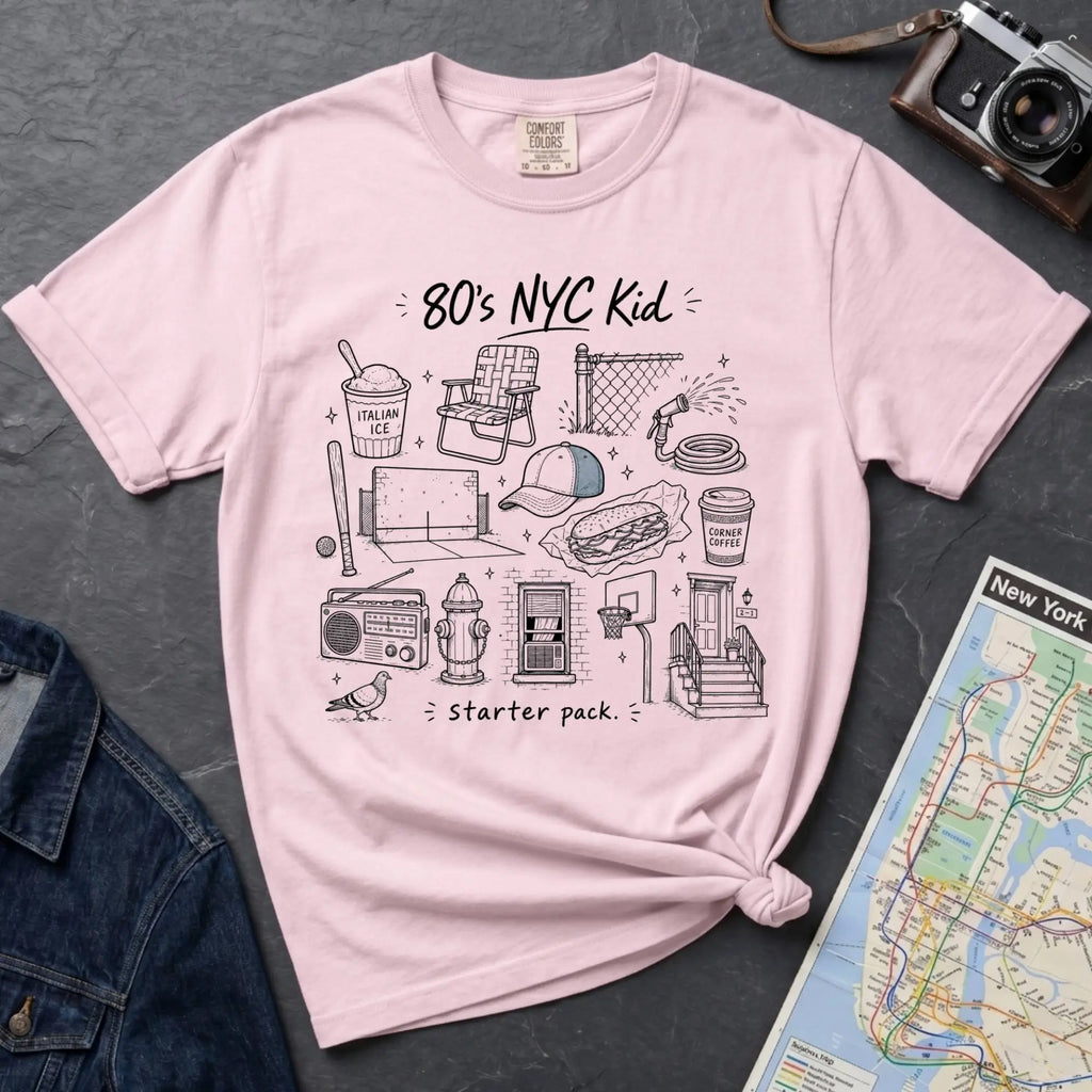 Pink Comfort Colors t-shirt featuring an 80’s NYC Kid Starter Pack graphic with hand-drawn New York City icons including Italian ice, a radio, stoop steps, stickball, a fire hydrant, and a pigeon.