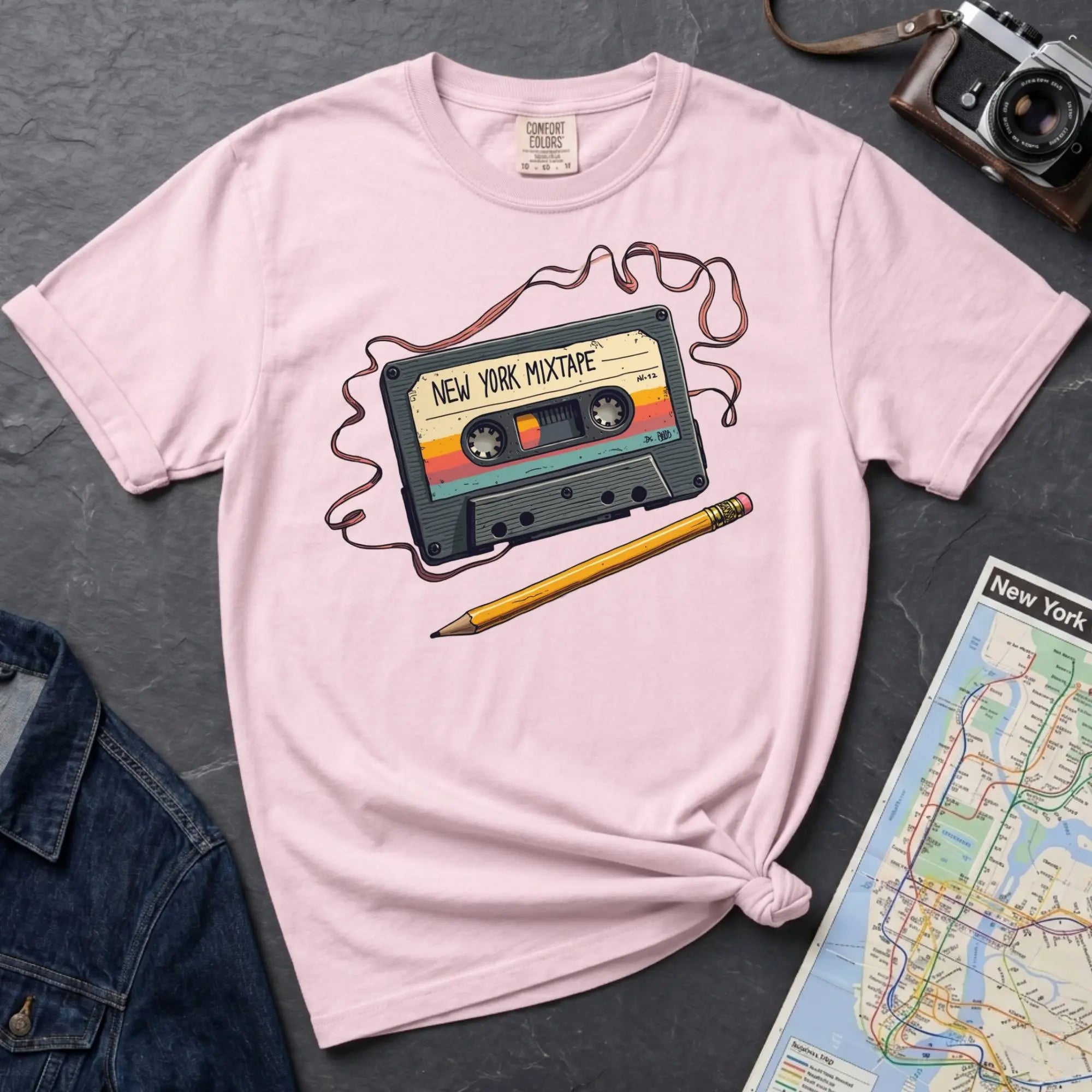 Pink t-shirt with a cassette tape graphic and pencil on a gray surface with a map and denim jacket.