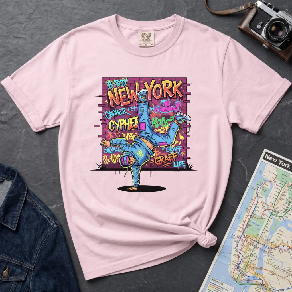 Pink t-shirt with a colorful graphic design featuring a breakdancer and text on a dark surface with a denim jacket and a map.