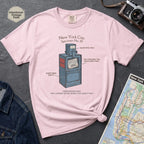 Pink t-shirt with a newspaper box graphic and text on a textured surface with a camera and map.