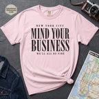 Pink Comfort Colors t-shirt featuring bold New York City “Mind Your Business, We’ll All Be Fine” text in a vintage black typography design.