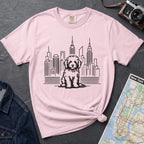 Pink t-shirt with a Golden Doodle dog and cityscape design on a gray surface with a map and camera.