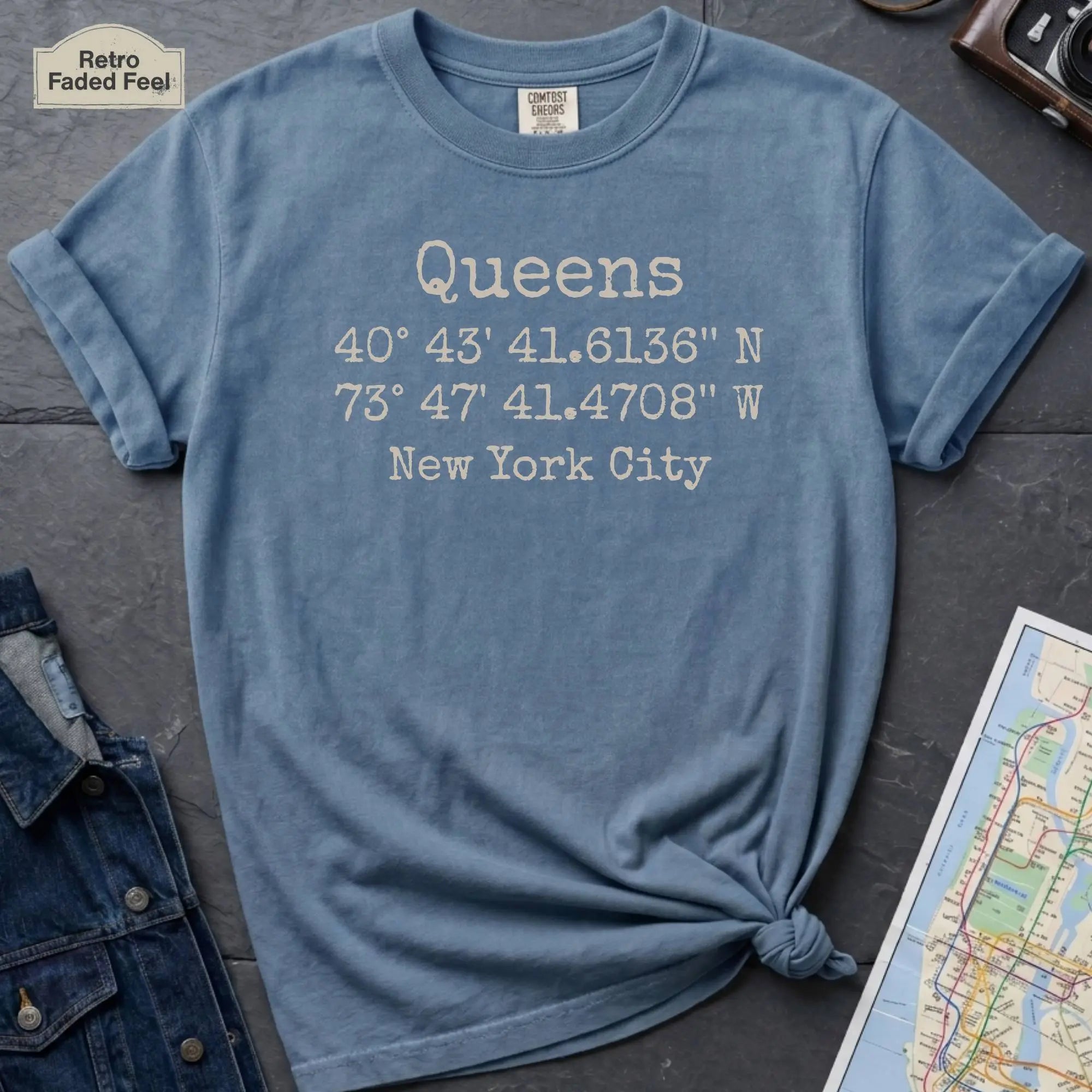 Blue Comfort Colors t-shirt featuring Queens, NY coordinates and New York City text in a minimalist typewriter-style design.