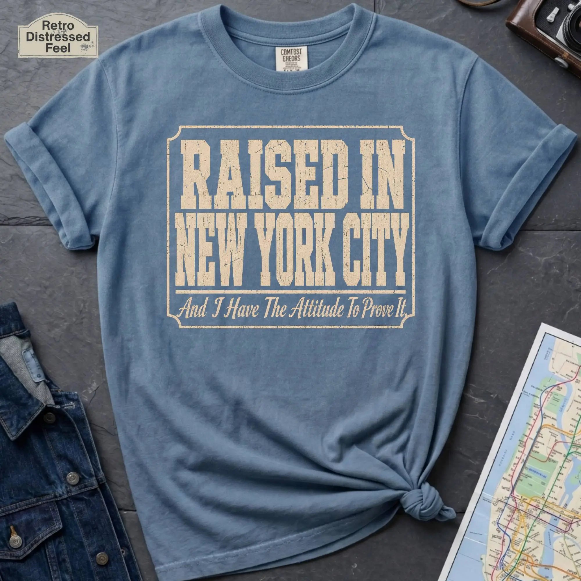 Blue Comfort Colors t-shirt featuring distressed vintage text that reads “Raised in New York City, And I Have the Attitude to Prove It.