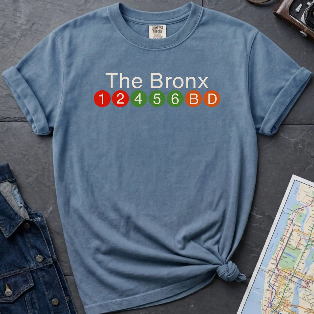 Blue Comfort Colors t-shirt featuring a minimalist Bronx subway line graphic with The Bronx text and colorful NYC train icons.