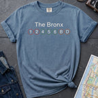 Blue t-shirt with 'The Bronx' and subway line numbers on a dark surface with a map and camera.