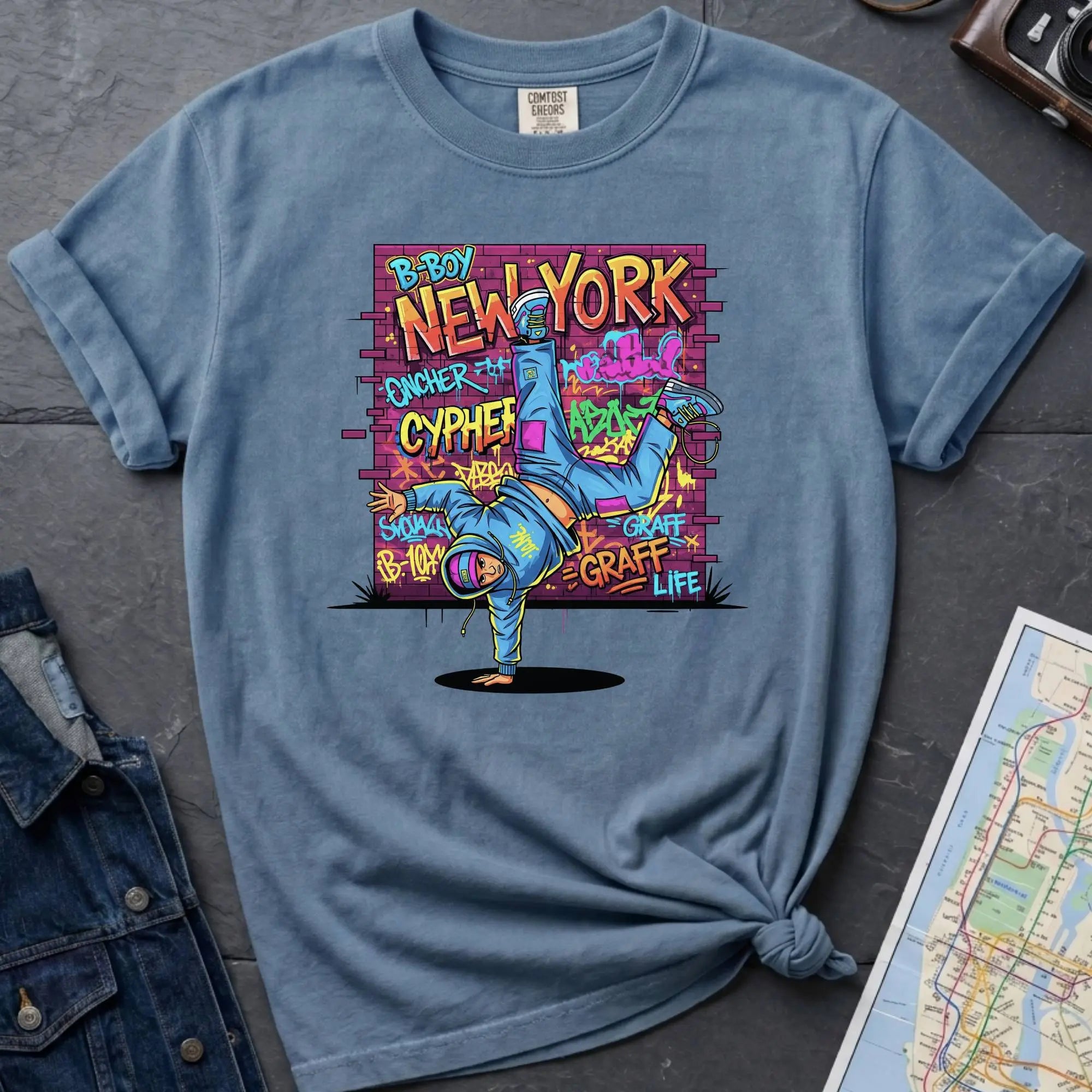 Blue Comfort Colors t-shirt featuring a colorful B-Boy New York graphic with a breakdancer in front of a graffiti brick wall.