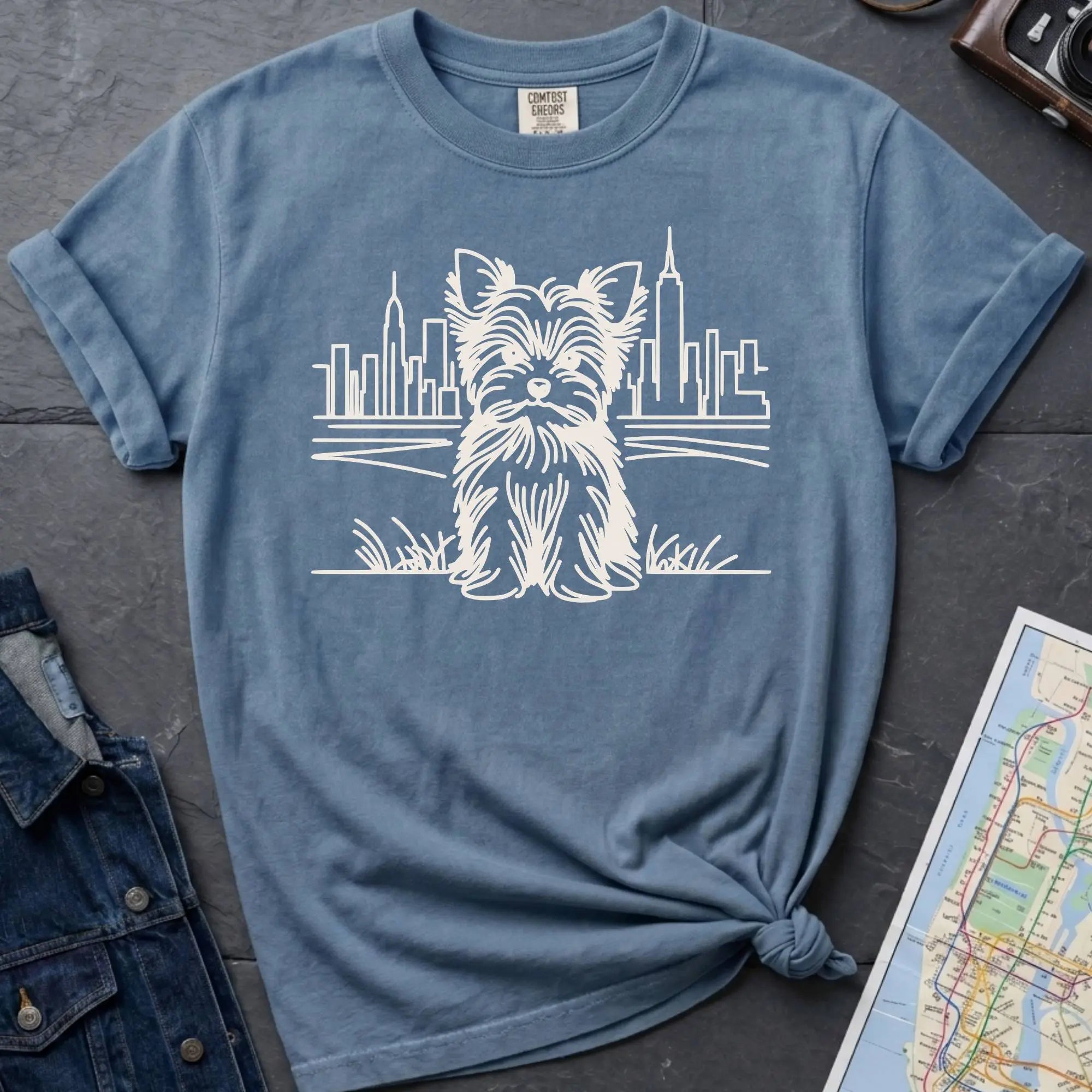 Blue Comfort Colors t-shirt featuring a minimalist Yorkshire Terrier (Yorkie) illustration in front of the New York City skyline.