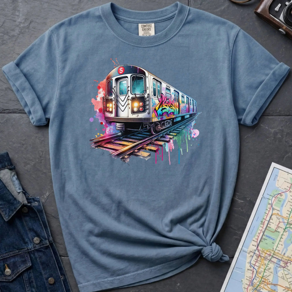 Blue Comfort Colors t-shirt featuring a colorful NYC subway train graphic with graffiti-style paint details and bright street art accents.