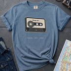 Blue t-shirt with cassette tape graphic and text on a gray surface with denim jacket and map.