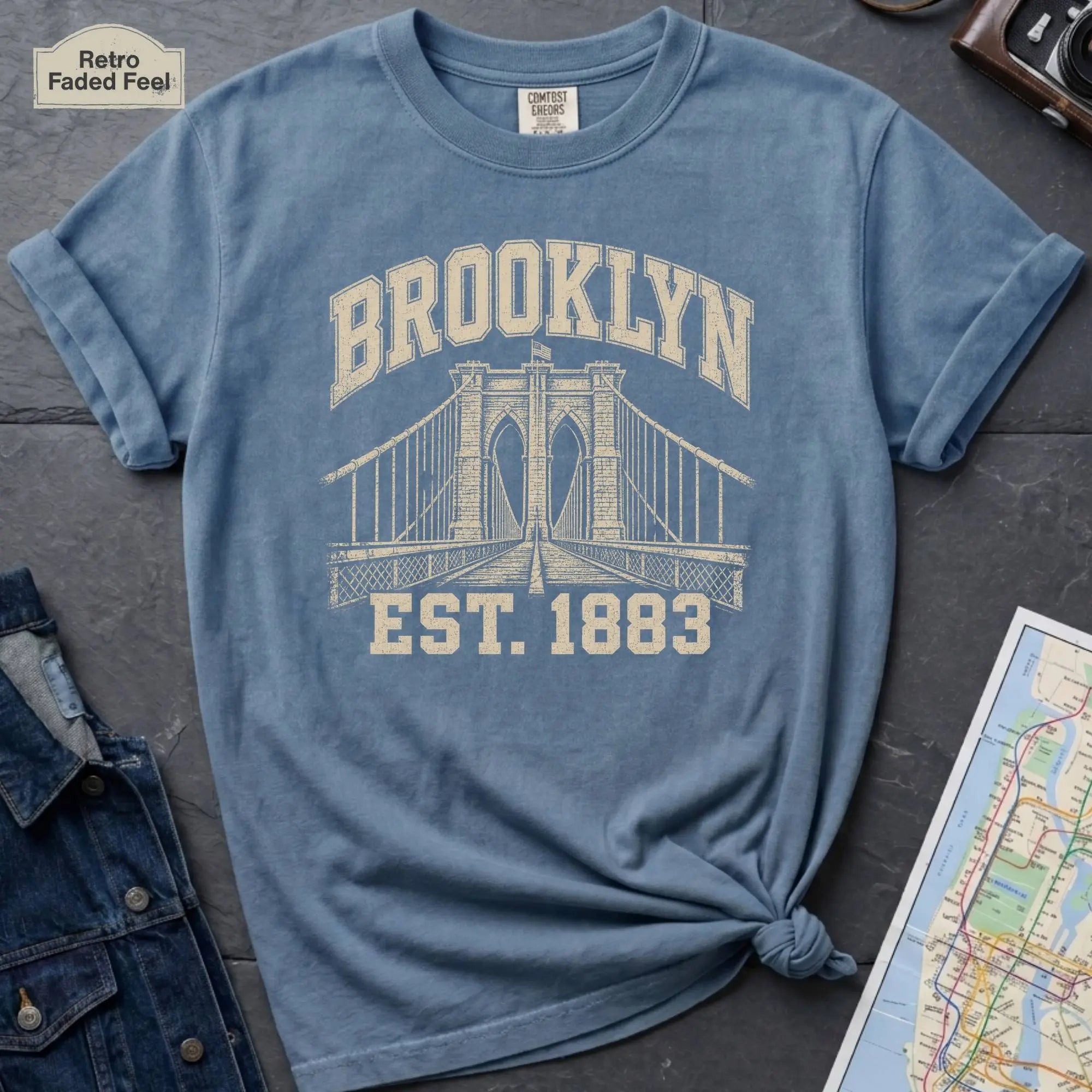 Blue Comfort Colors t-shirt featuring a vintage Brooklyn Bridge graphic with bold Brooklyn text and “Est. 1883” lettering.