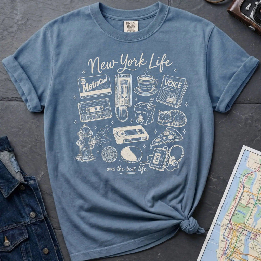 Blue Comfort Colors t-shirt featuring a New York Life Was the Best Life graphic with hand-drawn NYC nostalgia icons including a MetroCard, cassette tape, pay phone, coffee cup, newspaper, pizza slice, fire hydrant, Walkman, and bodega cat.
