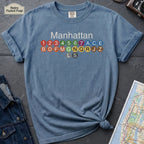 Blue Comfort Colors t-shirt featuring a minimalist Manhattan subway line graphic with colorful NYC train icons.