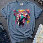 Blue t-shirt with a graphic of a person spray painting a colorful mural on a brick wall.