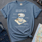 Blue t-shirt with New York City coffee cup graphic on a textured surface with map and camera.