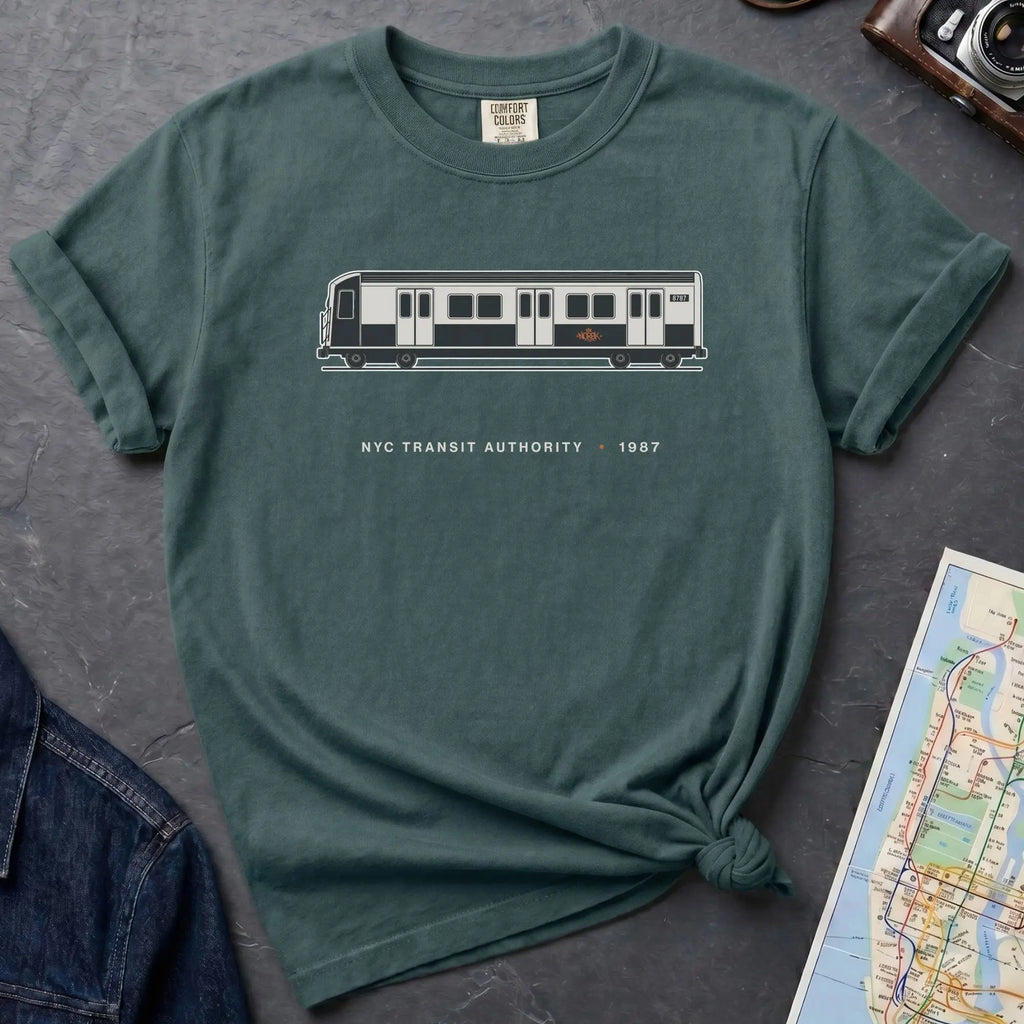 Blue Spruce Comfort Colors t-shirt featuring a minimalist New York City subway car graphic with “NYC Transit Authority • 1987” text.