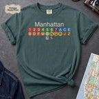 Blue Spruce Comfort Colors t-shirt featuring a minimalist Manhattan subway line graphic with colorful NYC train icons.
