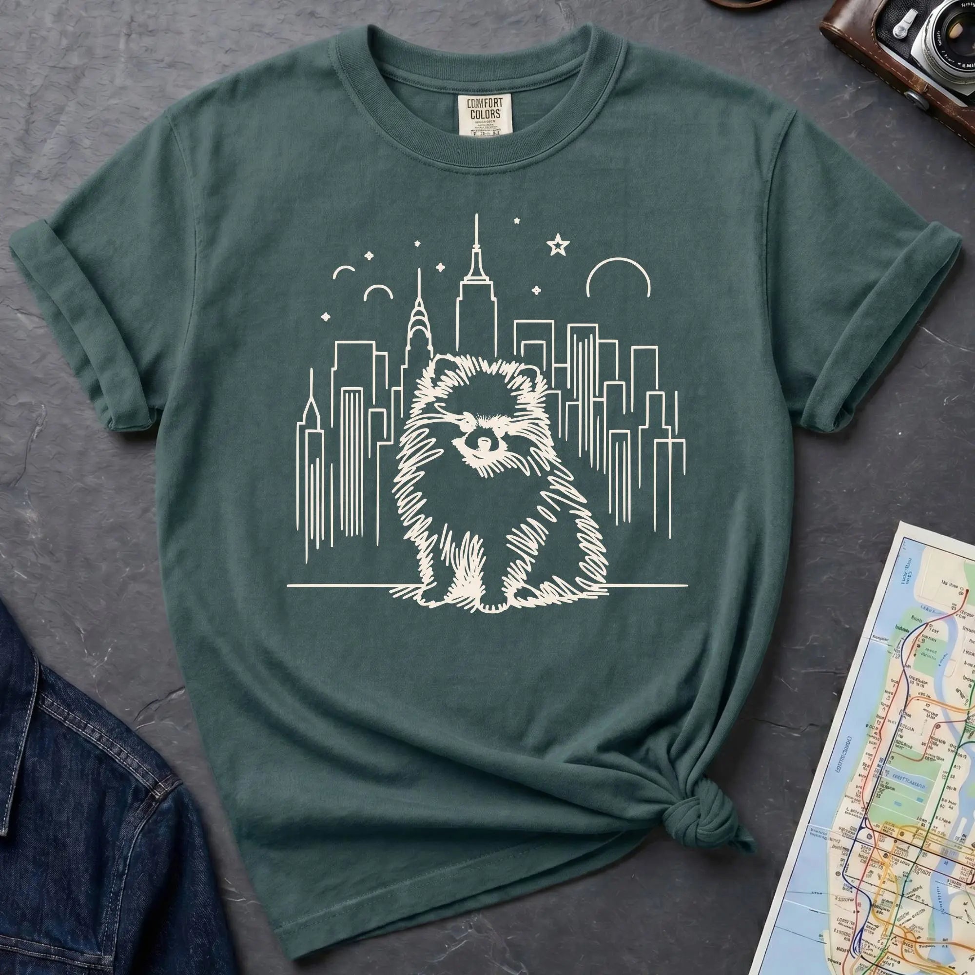 Blue Spruce Comfort Colors t-shirt featuring a fluffy small dog illustration in front of the New York City skyline.