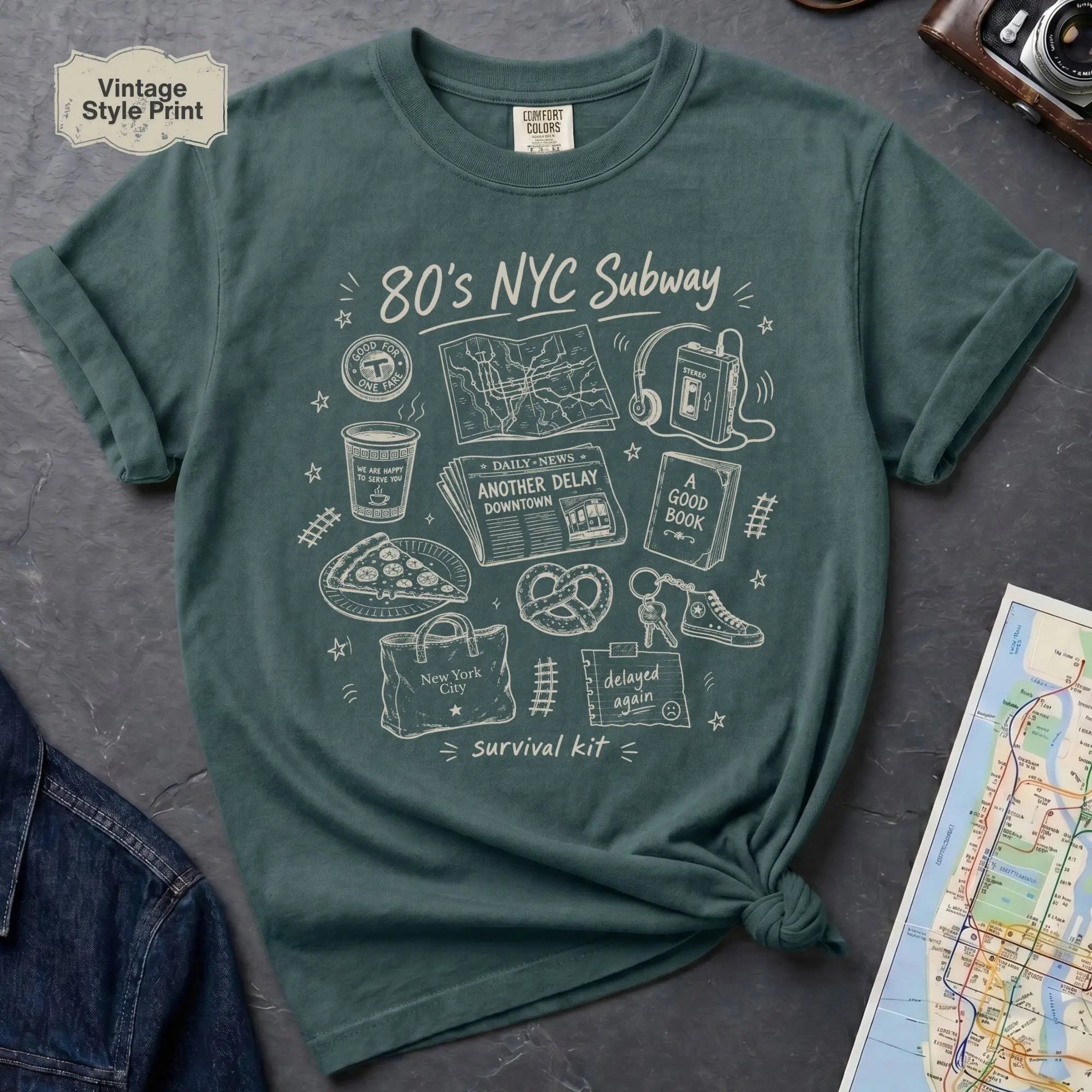 Blue Spruce t-shirt with '80s NYC Subway Survival Kit' graphic on a dark surface with a map and jeans.