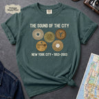 Blue Spruce Comfort Colors t-shirt featuring vintage New York City subway tokens with “The Sound of the City” and “New York City • 1953–2003” text.