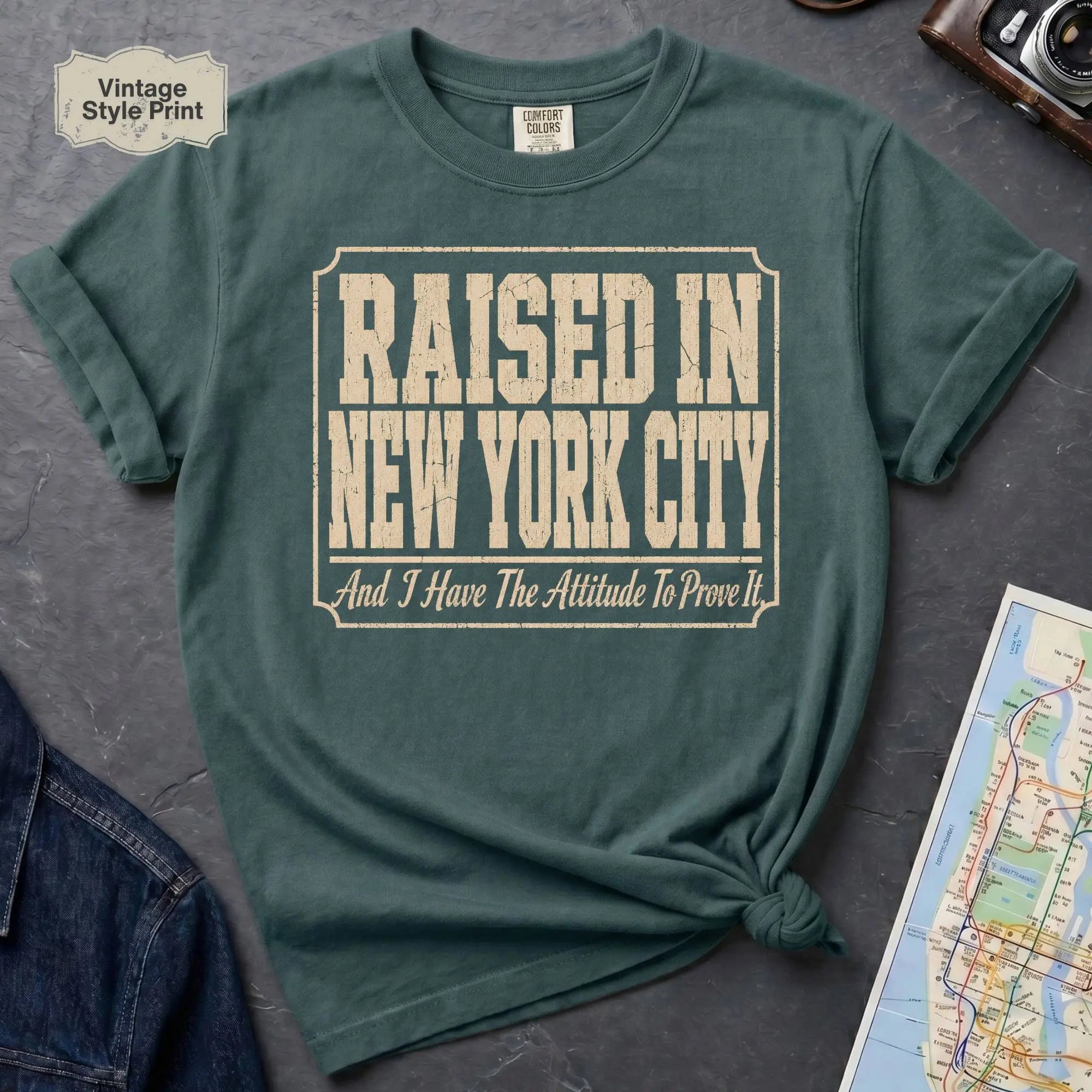 Blue Spruce Comfort Colors t-shirt featuring distressed vintage text that reads “Raised in New York City, And I Have the Attitude to Prove It.