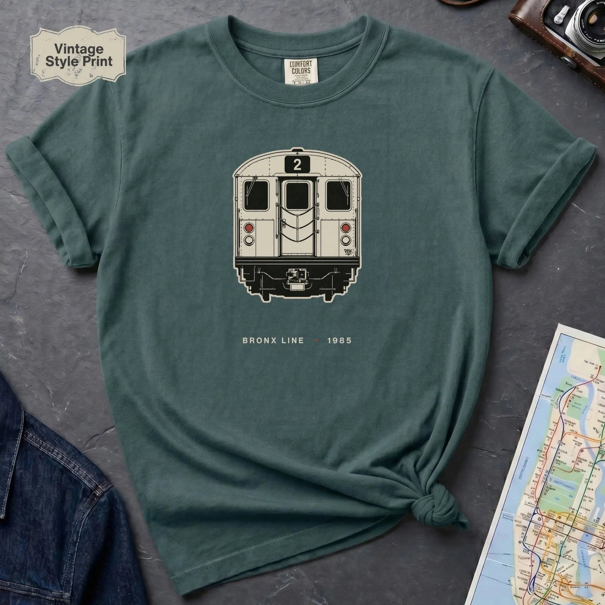 Blue Spruce colored t-shirt with a NYC subway train graphic on a dark surface with a map and a denim jacket.