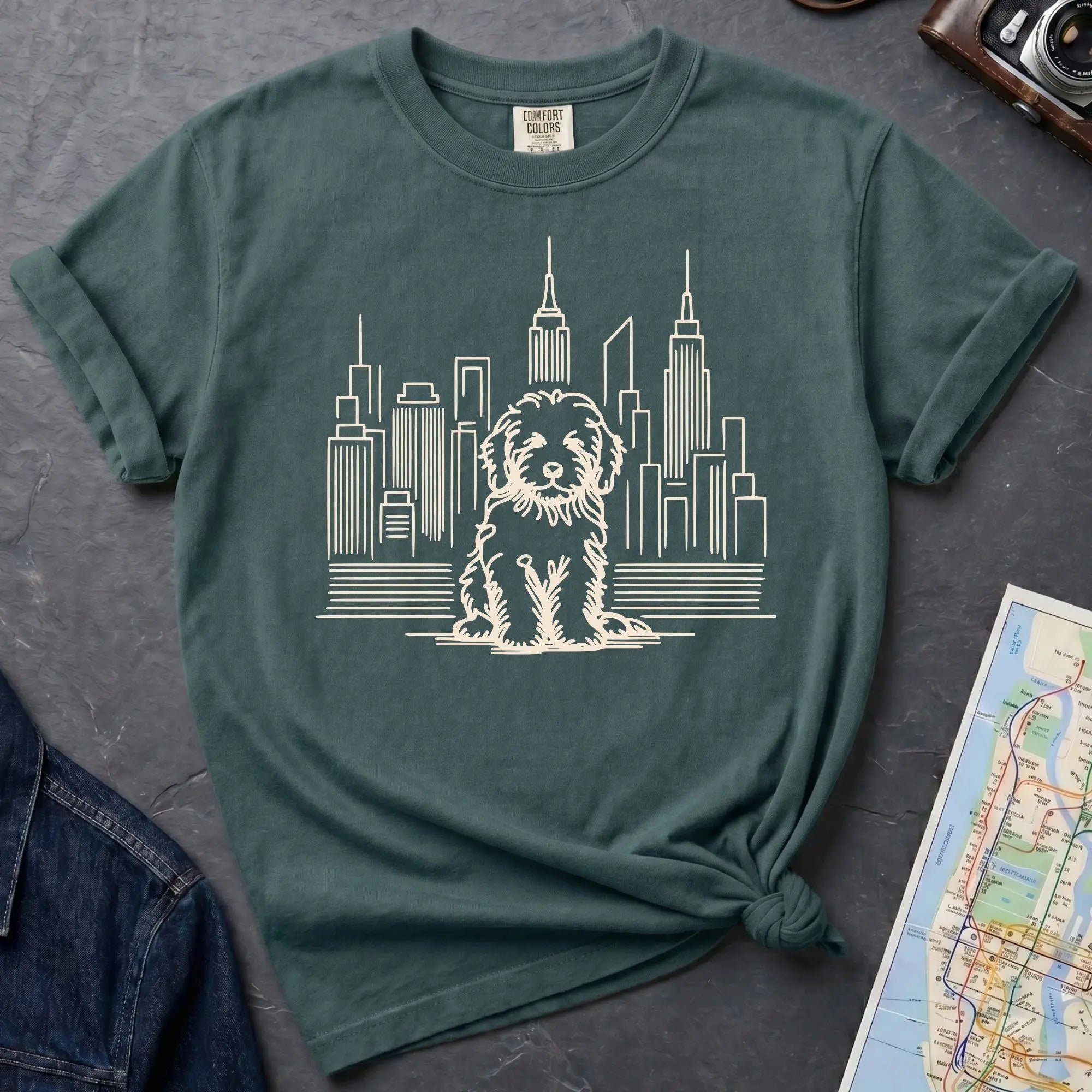 Blue Spruce t-shirt with a Golden Doodle and cityscape design on a dark surface with a map and camera.