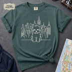 Blue Spruce t-shirt with a Maltese dog and cityscape design on a gray surface with a map and camera.