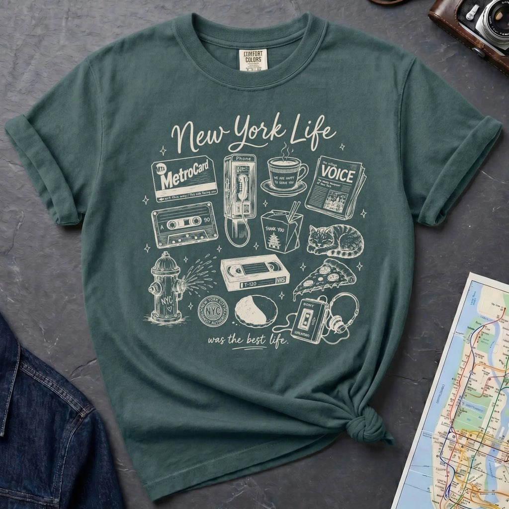 Blue Spruce Comfort Colors t-shirt featuring a New York Life Was the Best Life graphic with hand-drawn NYC nostalgia icons including a MetroCard, cassette tape, pay phone, coffee cup, newspaper, pizza slice, fire hydrant, Walkman, and bodega cat.