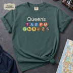 Blue spruce Black Comfort Colors t-shirt featuring a minimalist Queens subway line graphic with colorful NYC train icons.