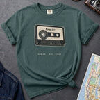 Blue spruce t-shirt with cassette tape graphic and text on a gray surface with denim jacket and map.