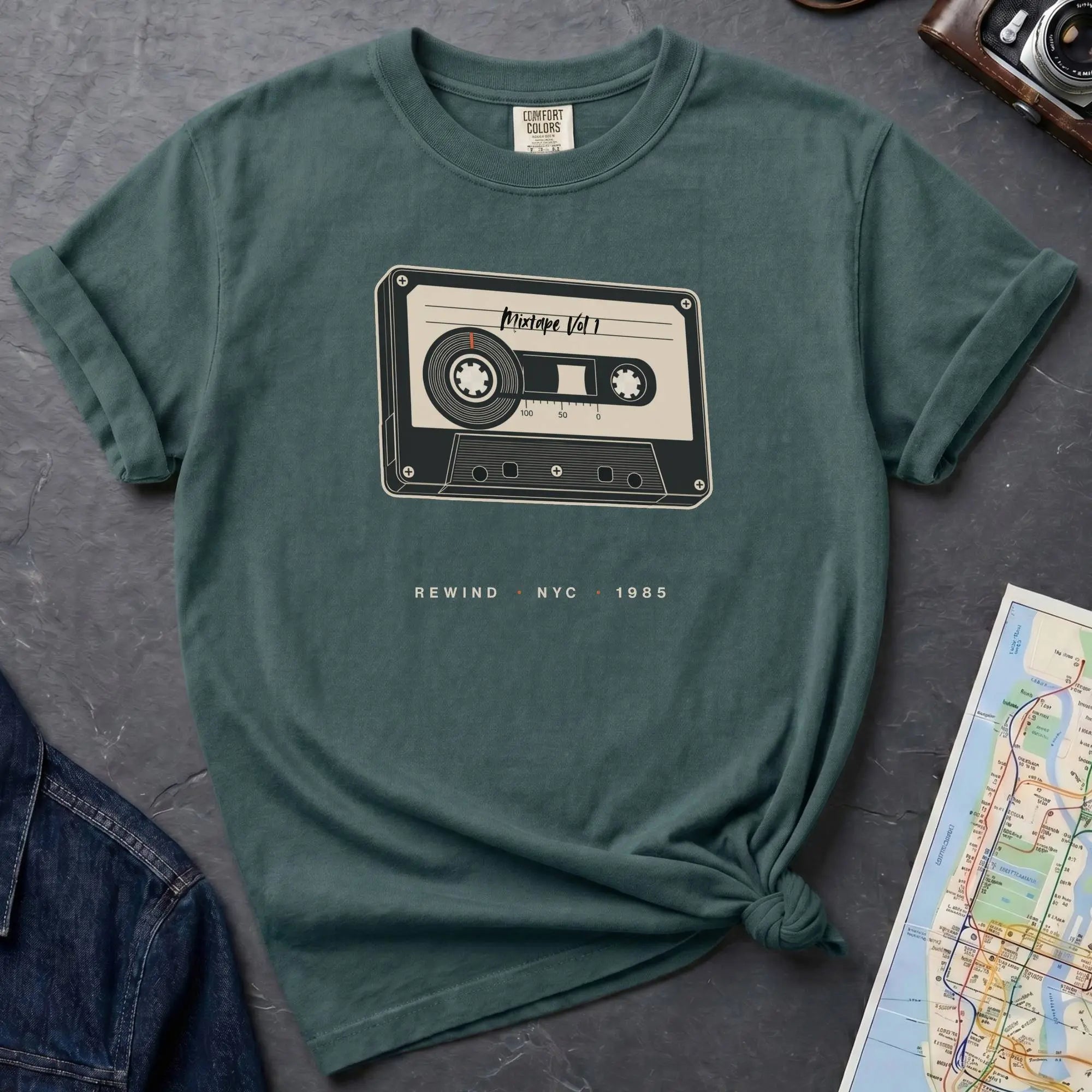 Blue spruce t-shirt with cassette tape graphic and text on a gray surface with denim jacket and map.