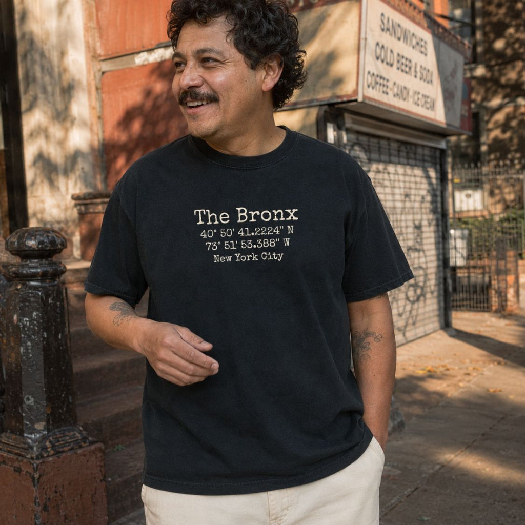 Man wearing a black Comfort Colors t-shirt with 'The Bronx' coordinates text, standing on a street.
