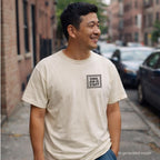 Man wearing an Ivory Comfort Colors T-shirt with black Canal Jean Co. NYC small front chest staff print, while standing on a NY sidewalk. 