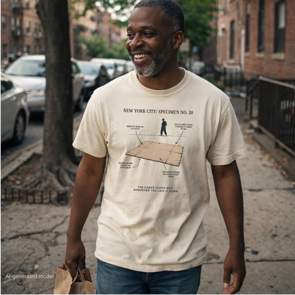 A man walking on a city sidewalk wearing an ivory Comfort Colors T-shirt with NYC breakdance cardboard specimen front print.