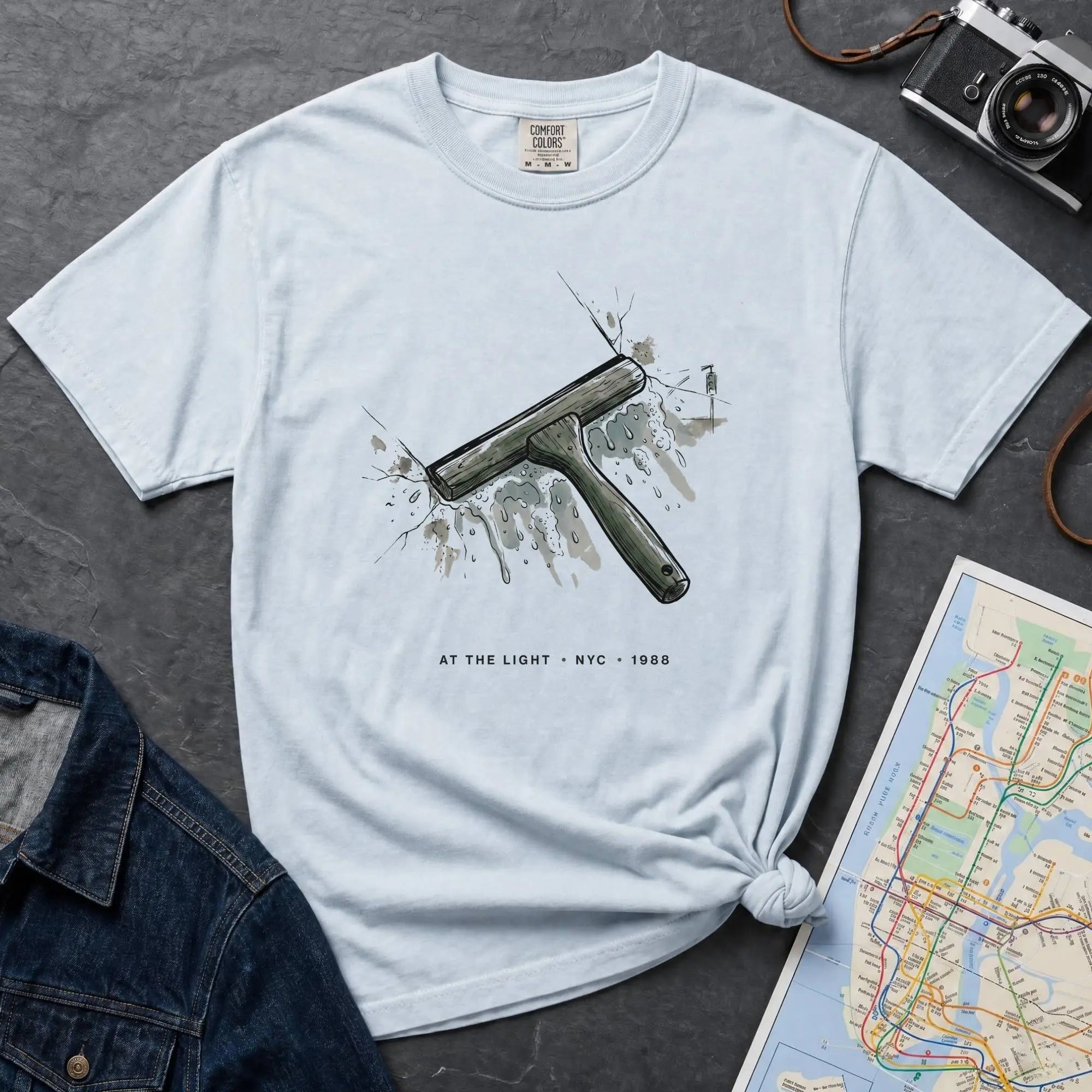 Light blue Comfort Colors t-shirt featuring a vintage windshield squeegee graphic with “At the Light • NYC • 1988” text.