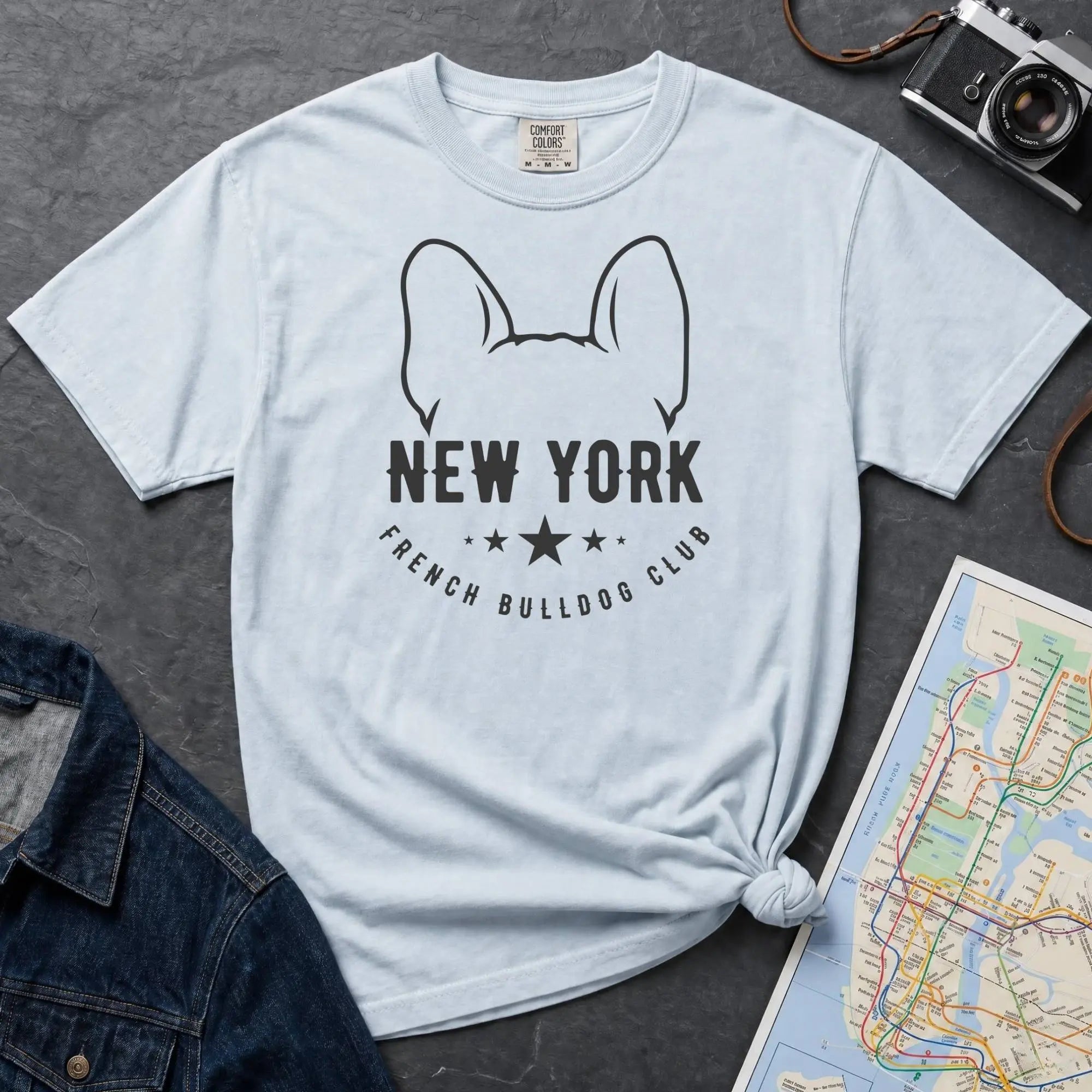 Light blue Comfort Colors t-shirt featuring a New York French Bulldog Club graphic with bold text, outlined French bulldog ears, stars, and a minimalist black design.