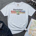Light blue Comfort Colors t-shirt featuring a minimalist Manhattan subway line graphic with colorful NYC train icons.