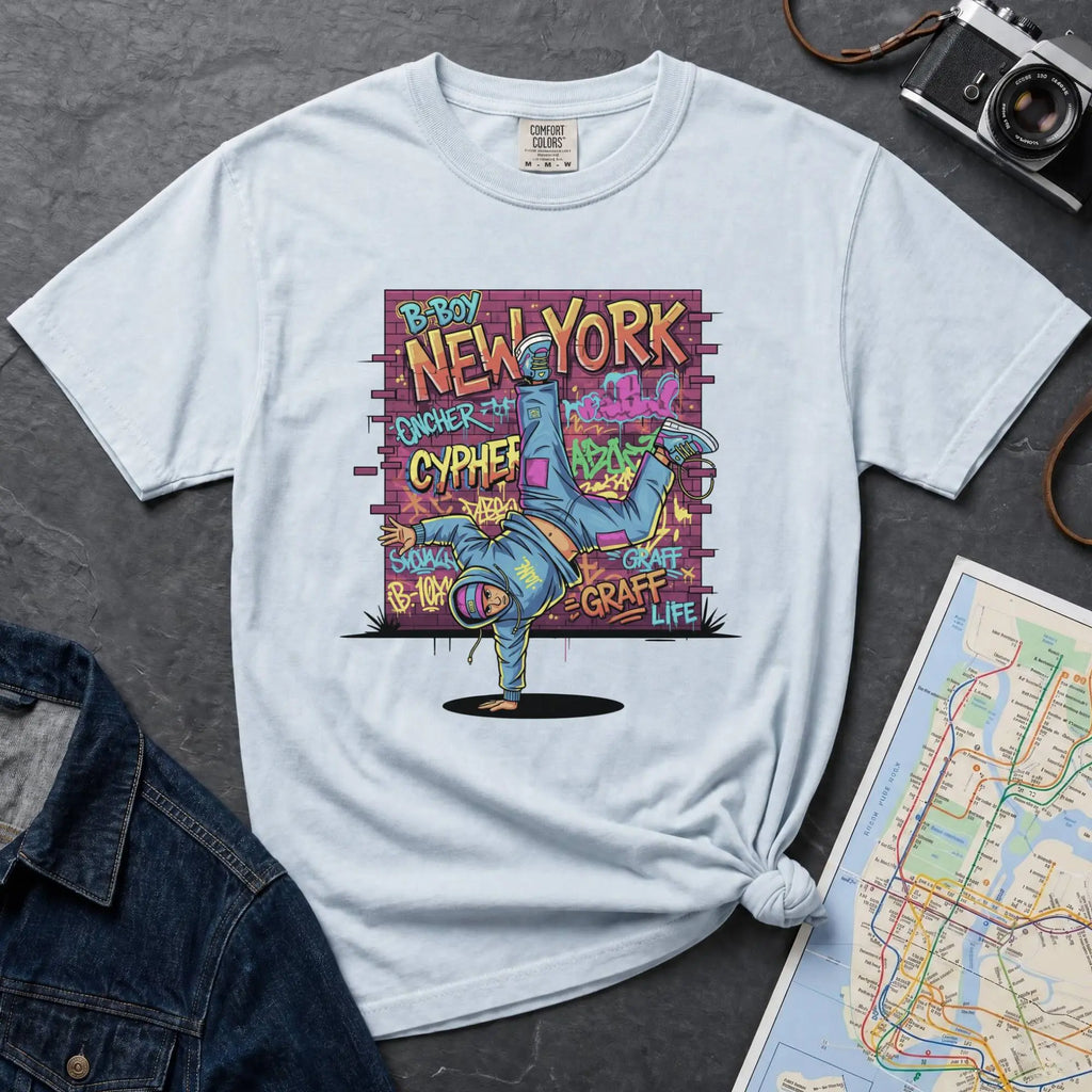 Light Blue t-shirt with a colorful graphic design featuring a breakdancer and text on a dark surface with a denim jacket and a map.