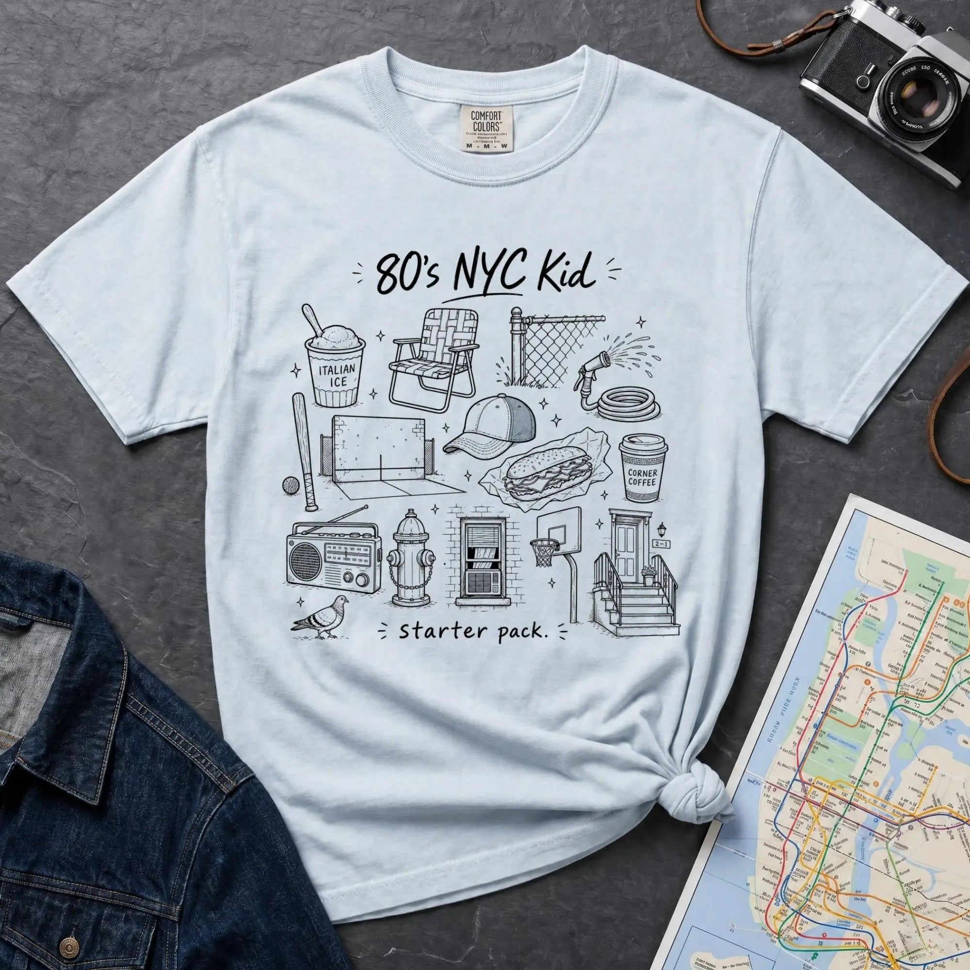 Light Blue Comfort Colors t-shirt featuring an 80’s NYC Kid Starter Pack graphic with hand-drawn New York City icons including Italian ice, a radio, stoop steps, stickball, a fire hydrant, and a pigeon.