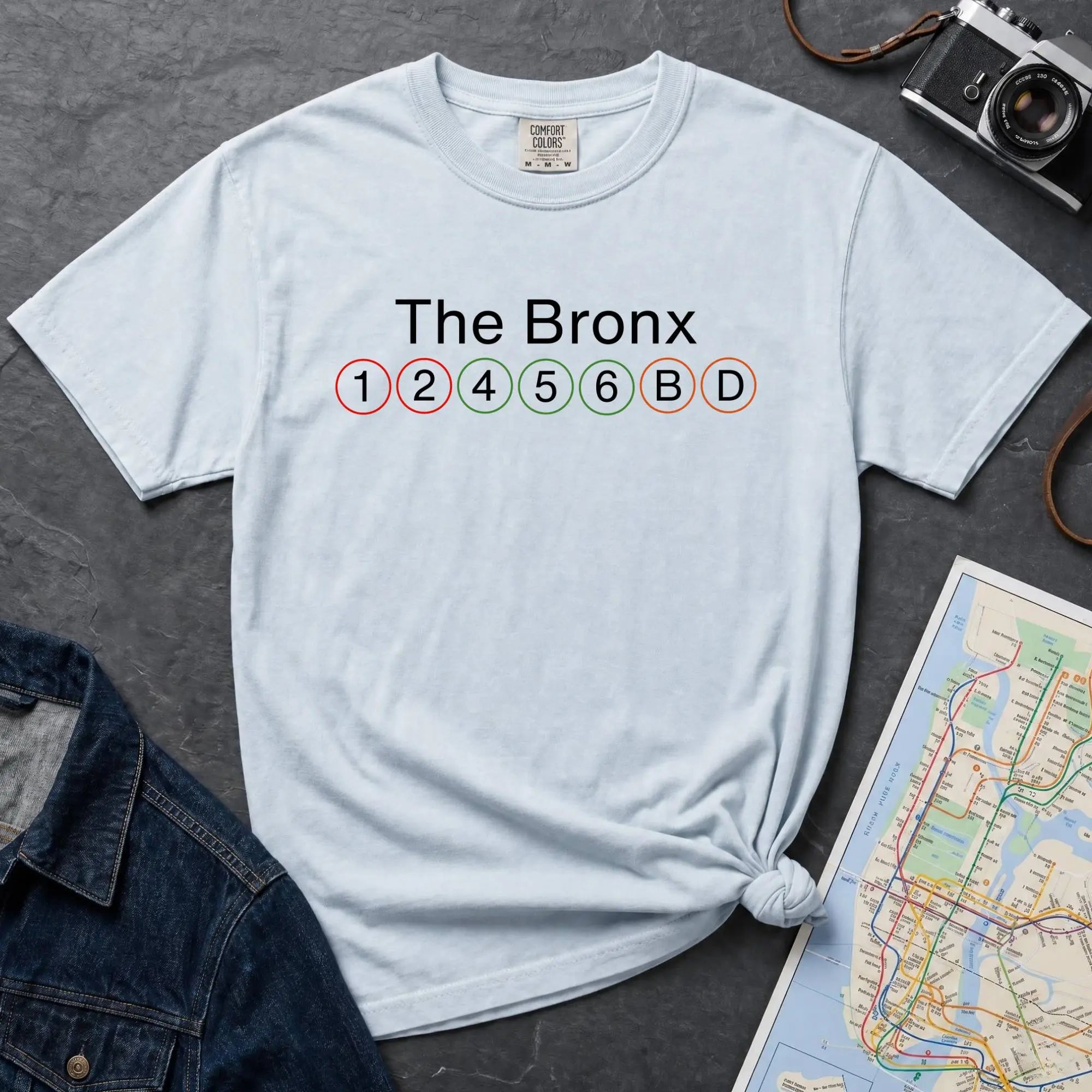 Light blue Comfort Colors t-shirt featuring a minimalist Bronx subway line graphic with The Bronx text and classic NYC train icons.
