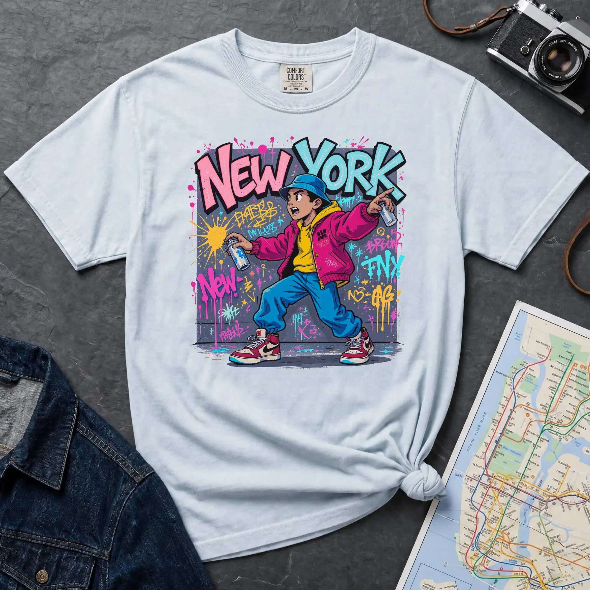 Light blue Comfort Colors t-shirt featuring a colorful NYC graffiti-style New York graphic with a young street artist holding a spray paint can