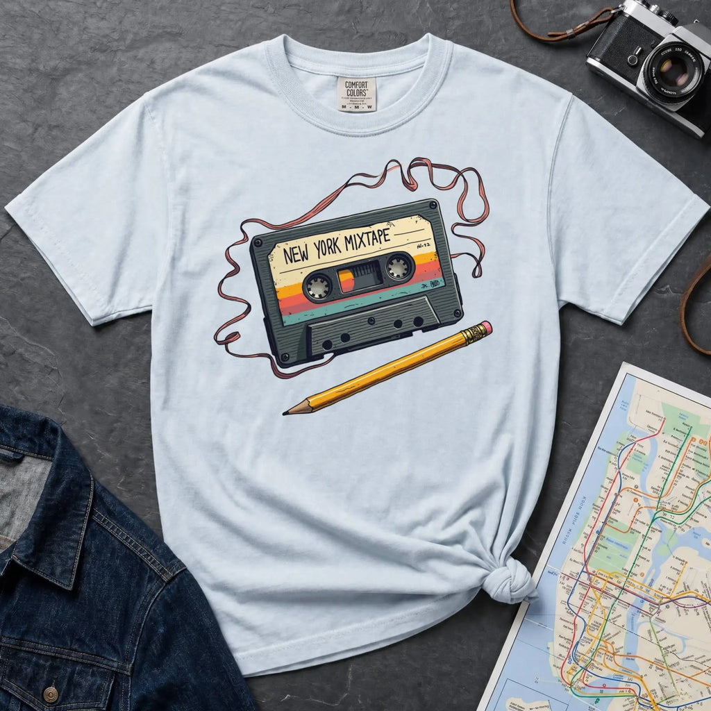 Light blue t-shirt with a cassette tape graphic and pencil on a gray surface with a map and denim jacket.