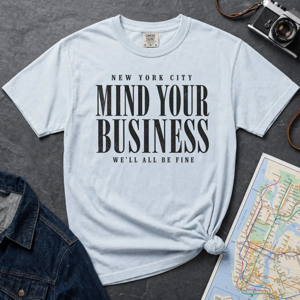Light blue Comfort Colors t-shirt featuring bold New York City “Mind Your Business, We’ll All Be Fine” text in a vintage black typography design.