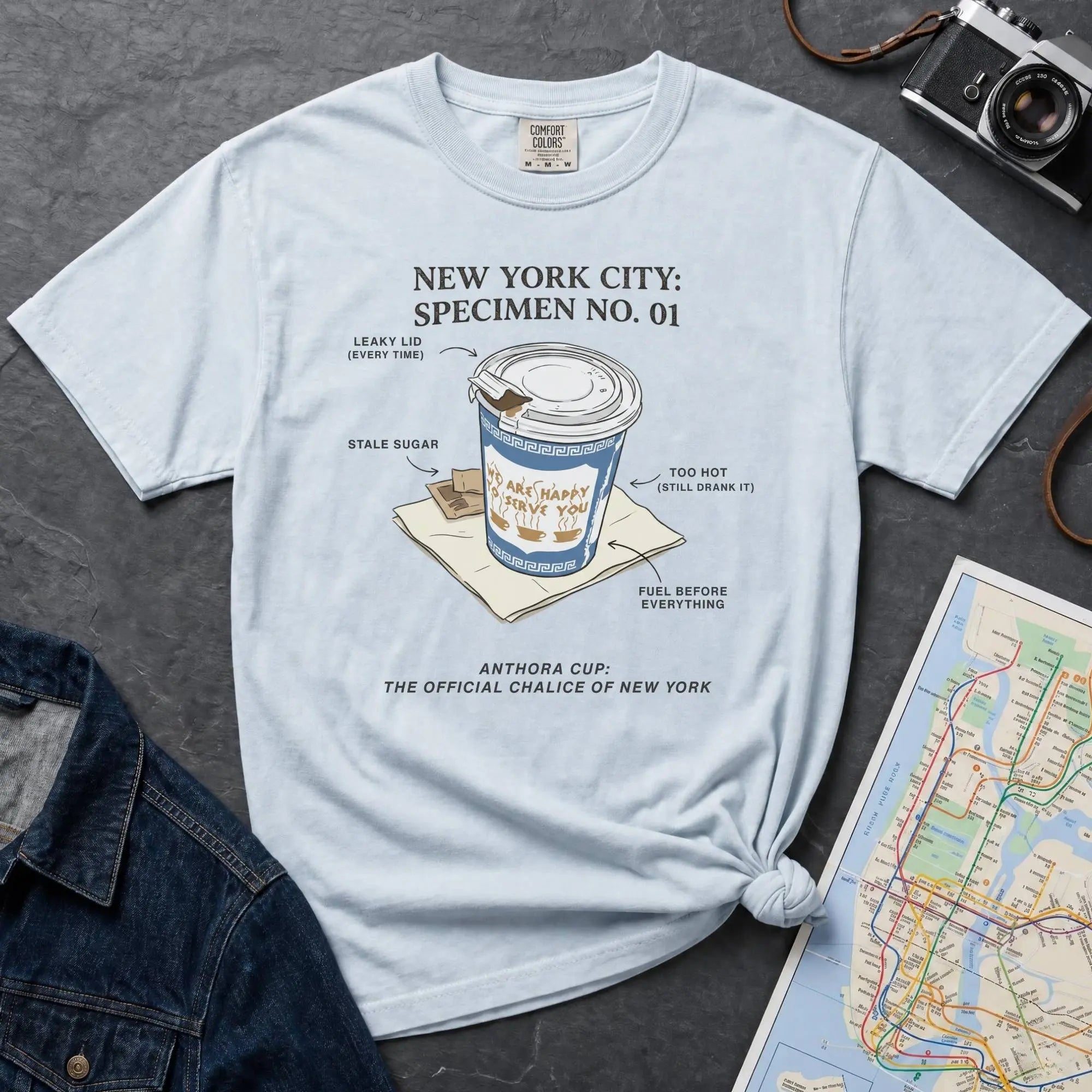 Light blue Comfort Colors t-shirt featuring a vintage New York City Anthora coffee cup graphic with specimen-style callouts and “The Official Chalice of New York” text.